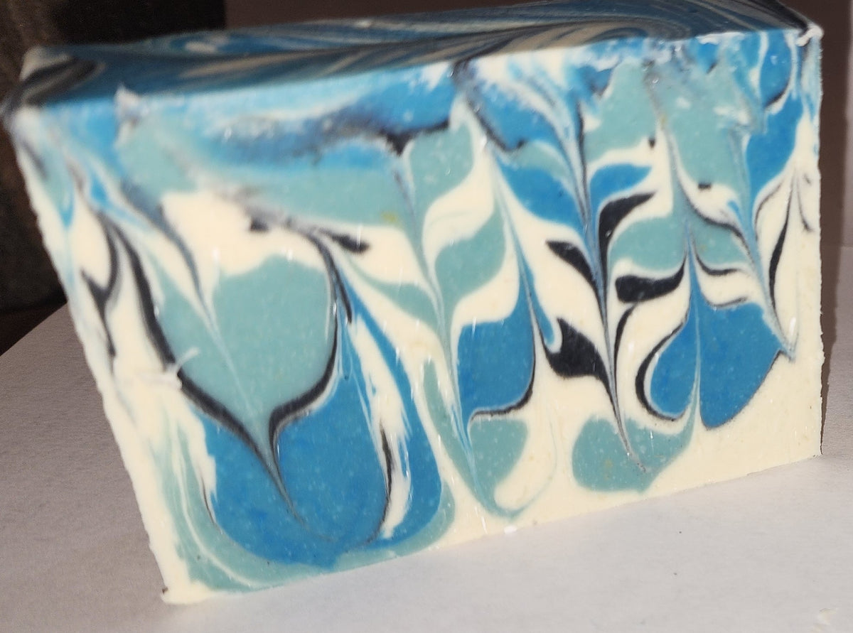 Iced Berries goat milk soap: a rectangular bar of handmade soap with a marbled swirl pattern in shades of blue, light aqua, white, and black, resting on a white surface.