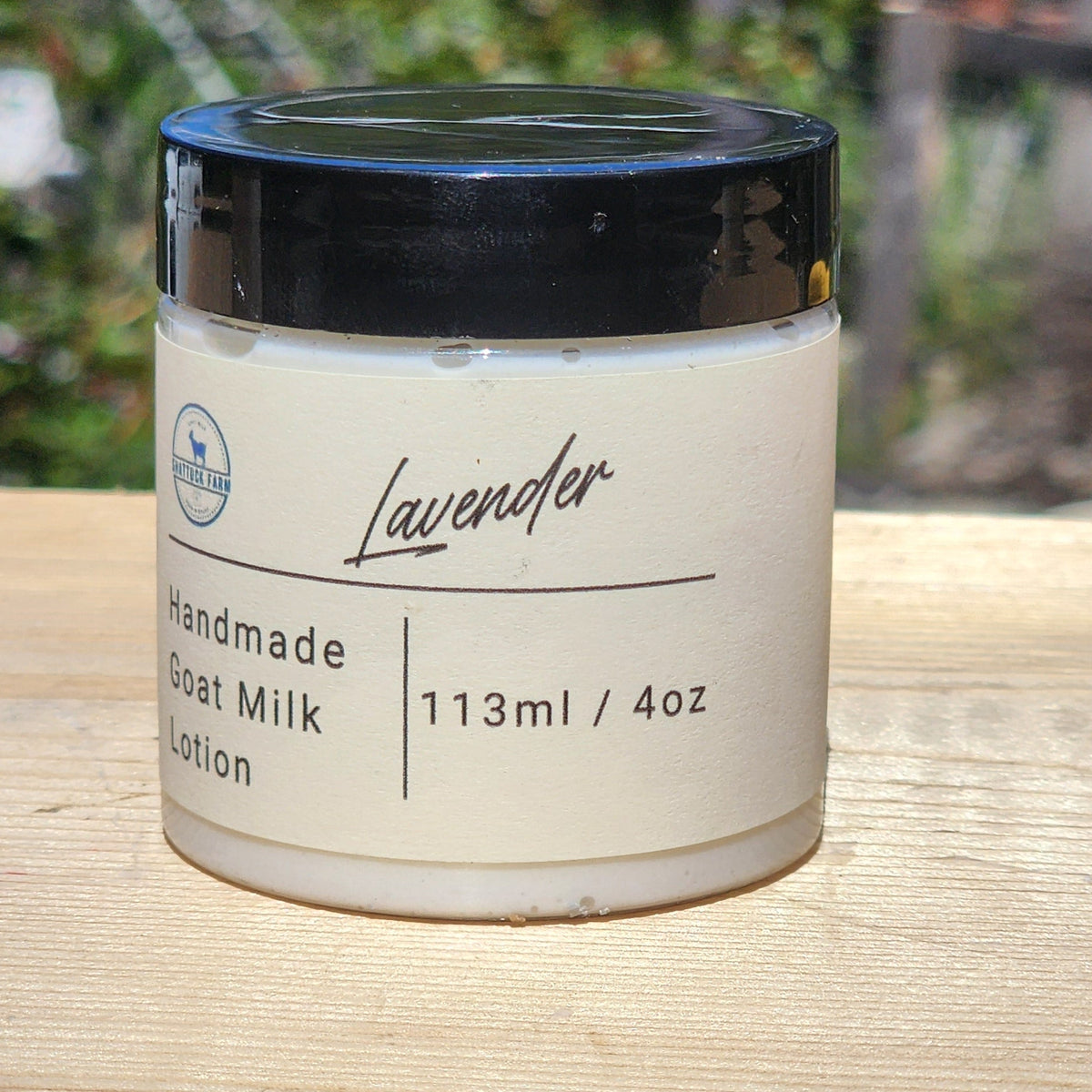 Jar of lavender handmade goat milk lotion on a wooden surface with a blurred natural background