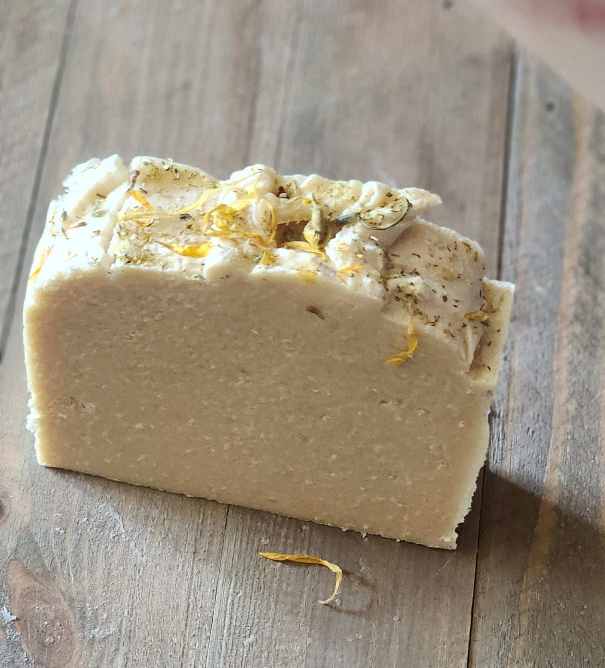 Bar of soap with visible herbs on a wooden surface