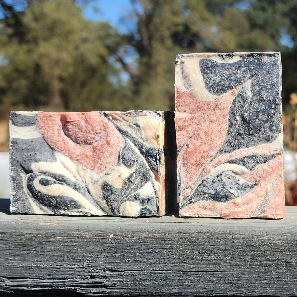 Bramble & Blossom goat milk soap: two marbled soap bars with pink, black, and white patterns on a wooden surface.