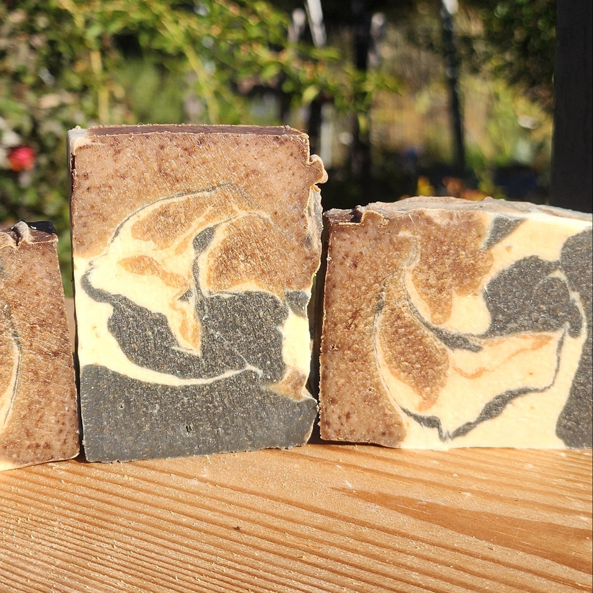 Three marbled soap bars on a wooden surface with a blurred natural background