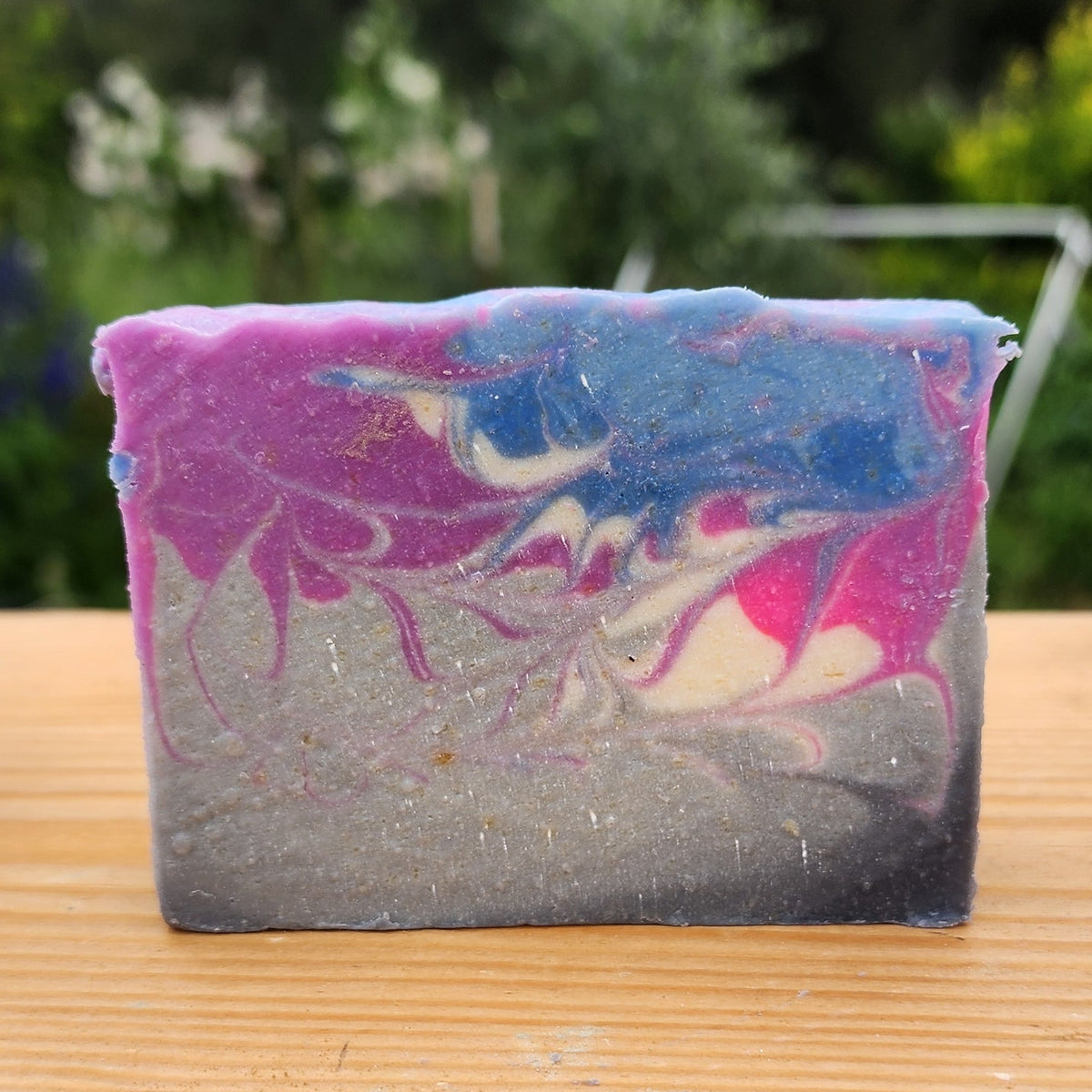 Colorful soap on a wooden surface with blurred greenery in the background