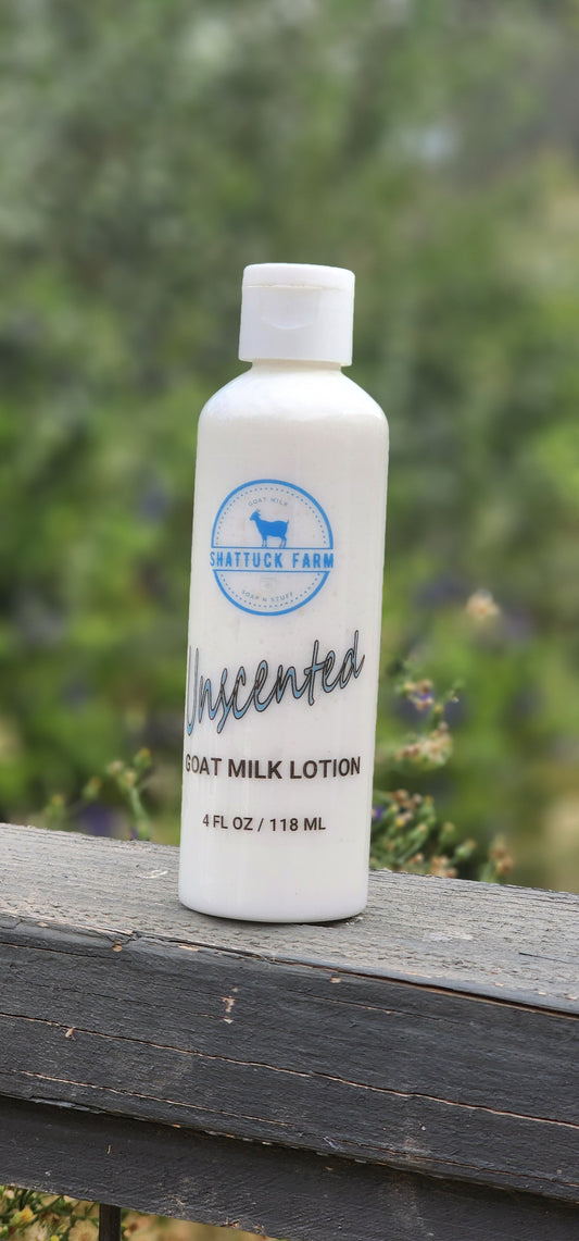 A white bottle of Shattuck Farm Unscented Goat Milk Lotion resting on a weathered wooden fence with a blurred green outdoor background.