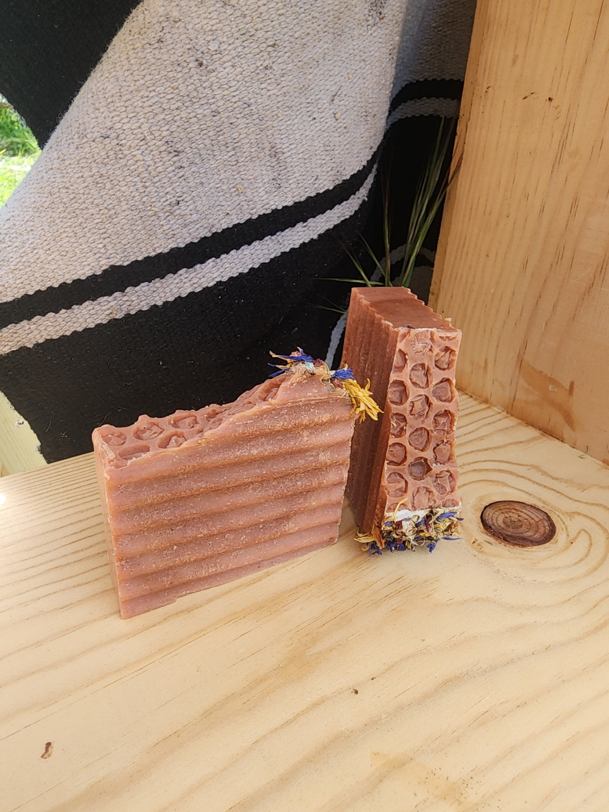 Honey Peppermint goat milk soap: two handmade bars with honeycomb and wavy patterns in a dusty pinkish-brown color, decorated with dried flower petals, displayed on a light wood surface.