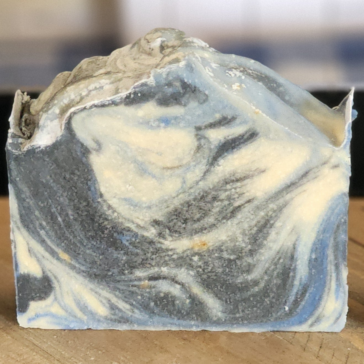 The Perfect Man goat milk soap: one bar with swirls of charcoal gray, pale blue, and cream, on a wooden surface.