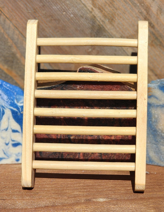 Light wooden soap dish with slatted rails, standing upright in front of a bar of soap, with blue and white marbled soap bars on either side